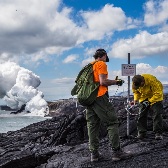 rangers work to establish viewing area on lava. steam plume in background.